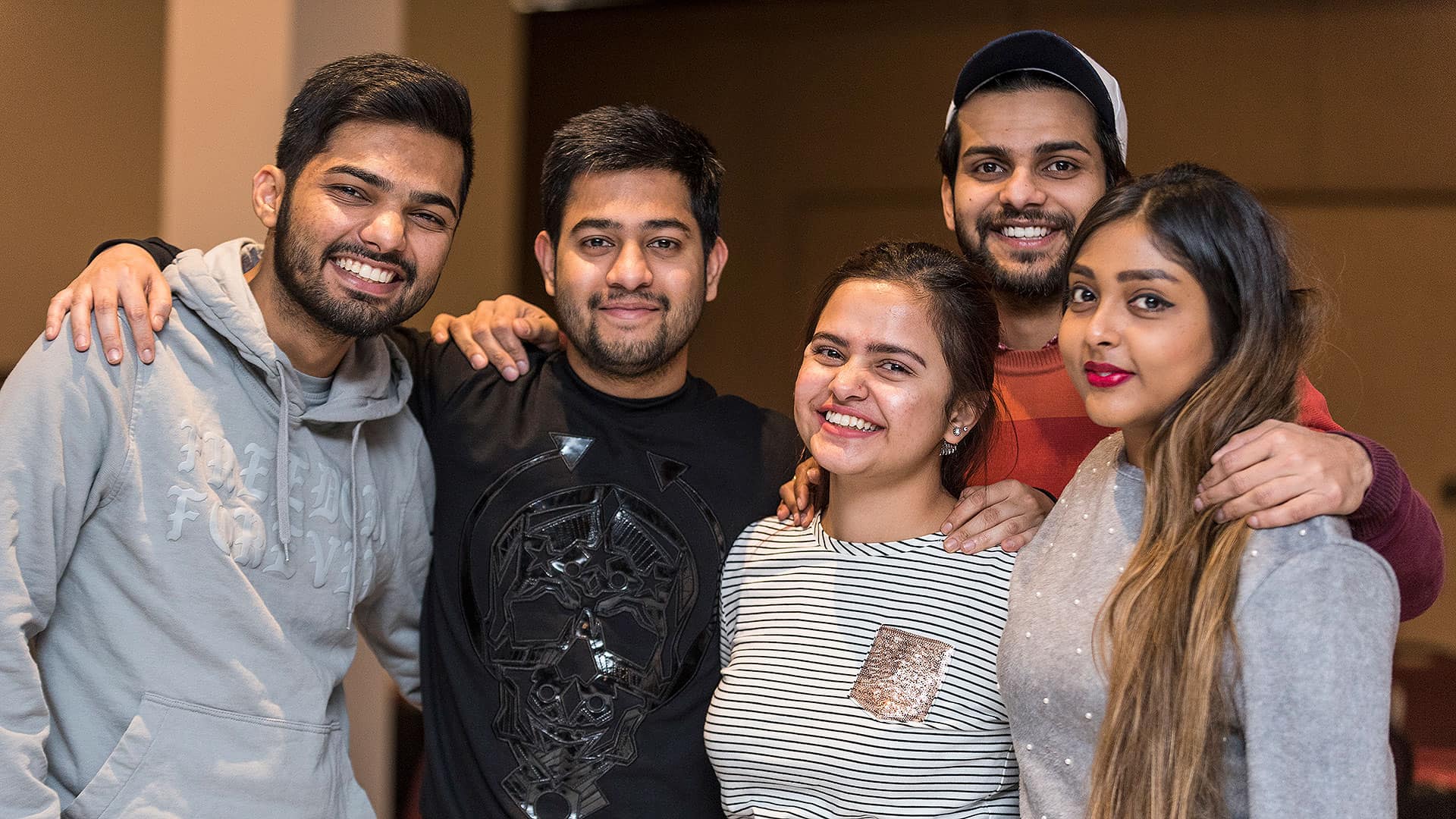 A photo of five young people with their arms around each other's shoulders