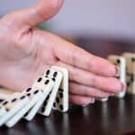 A hand stops the dominos from falling.