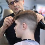 A man gives a teenager a haircut.