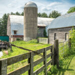 A photo of a farmer and silo at the end of a fence on a summer day.